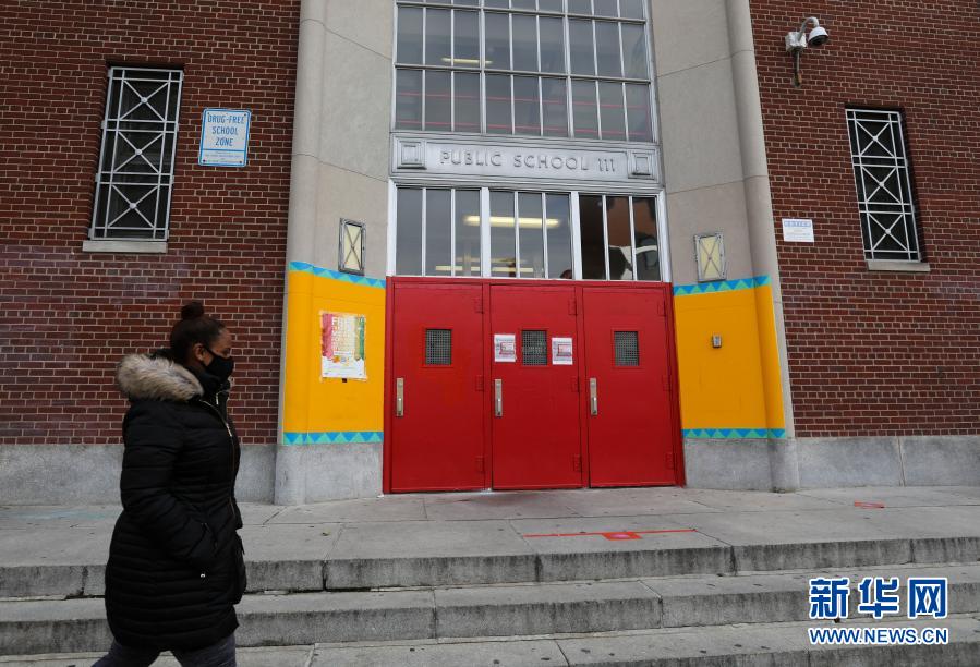 11月19日，在美国纽约，一名女子从一所公立学校外走过。纽约市长德布拉西奥18日宣布，纽约市公立学校19日起暂停线下授课，改为在线教学。新华社记者王迎摄