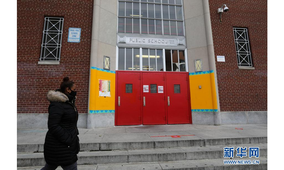 11月19日，在美国纽约，一名女子从一所公立学校外走过。纽约市长德布拉西奥18日宣布，纽约市公立学校19日起暂停线下授课，改为在线教学。新华社记者王迎摄