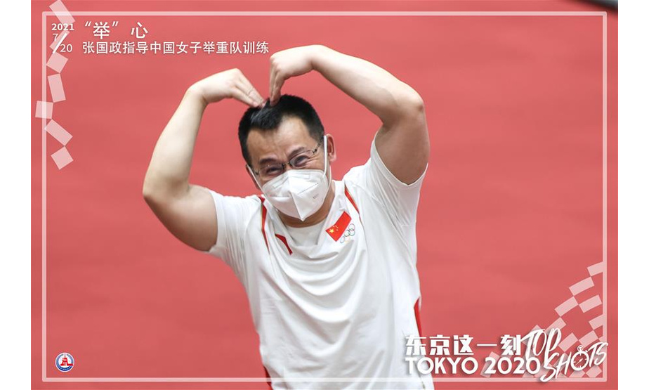 7月20日，中国女子举重队主教练张国政在热身训练中比心。 新华社记者 杨磊 摄 制图：马平