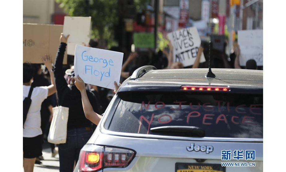 5月30日，在美国纽约昆斯区，一名示威者高举写着死亡非裔男子的名字“乔治·弗洛伊德”的牌子。 新华社记者 王迎 摄