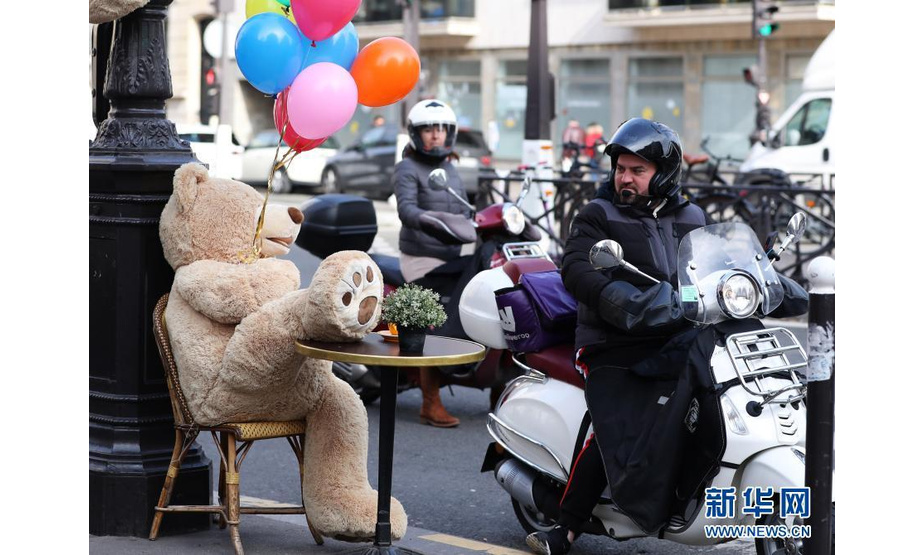 3月3日，一名男子骑摩托车经过法国巴黎街头一家餐馆外的玩具熊。3日，法国巴黎街头一家提供外带服务的餐馆被玩具熊“占领”，他们摸高爬低、四仰八叉“享受”阳光和美酒，引得路人驻足观看。受新冠肺炎疫情影响，法国餐馆、酒吧等场所自去年10月30日起一直关闭至今，不少餐馆推出外带服务。新华社记者 高静 摄