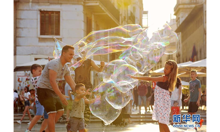 7月14日，在西班牙巴伦西亚，孩子们在一处广场上玩肥皂泡。 西班牙巴伦西亚紧靠大海，一年四季气候宜人。时值盛夏，游客纷纷来到这里度假，与当地居民一起享受悠闲夏日。 新华社记者 郭求达 摄