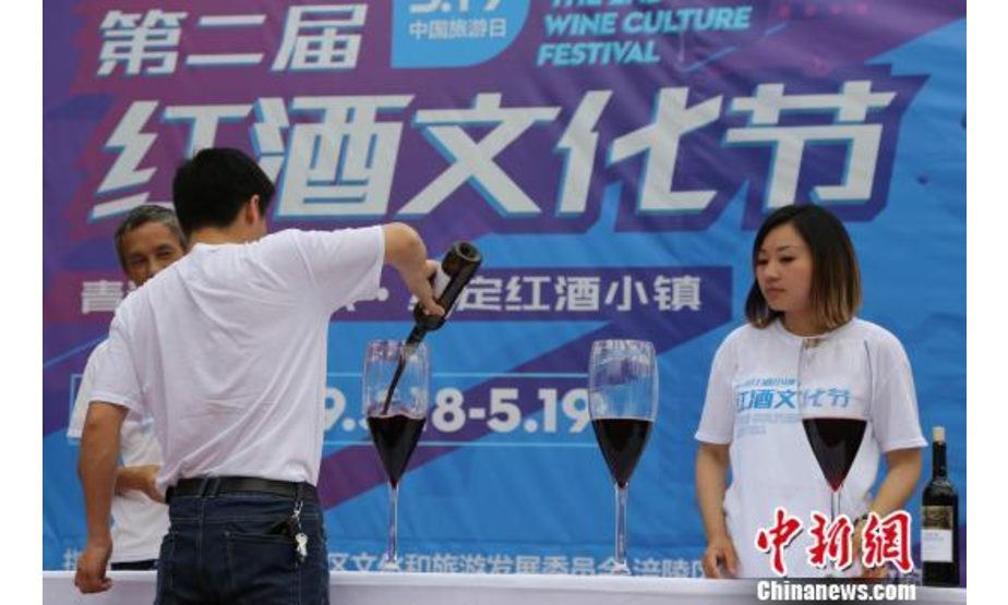 图为工作人员正在进行倒酒。 杨孝永 摄　　5月19日是中国旅游日，重庆涪陵红酒小镇景区举办了一场红酒文化节。其中，喝红酒比赛环节吸引不少游客前来报名参加。游客拿起巨型红酒杯，4人为一组，以最快速度喝完杯中红酒的选手为获胜者。