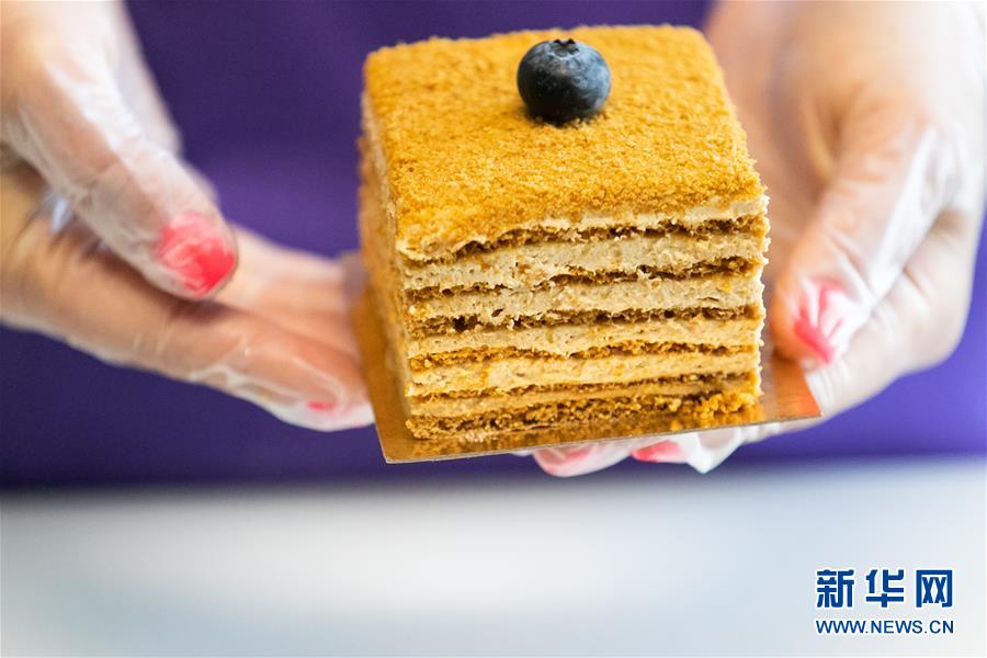 8月28日，在俄罗斯首都莫斯科，糕点师尤利娅展示制作完成的俄式蜂蜜蛋糕。俄式蜂蜜蛋糕是一种由蜂蜜、鸡蛋、面粉、牛奶等原料制成的多层蛋糕，深受喜爱甜食的俄罗斯人青睐。传统蜂蜜蛋糕的制作流程比较繁琐，首先将多种原料充分搅拌揉成面团，分别制作每一层蛋糕胚，然后将打发的奶油抹在烤好的蛋糕胚上，层层叠加起来，最后撒上蛋糕胚边角打成的碎屑即成。相传，沙皇亚历山大一世的妻子伊丽莎白不吃含有蜂蜜的食物，一位新来的厨师不了解她的习惯，为其制作了蜂蜜蛋糕，却深得皇后的喜爱，蜂蜜蛋糕从此成为闻名全俄的甜点。新华社记者 白雪骐 摄