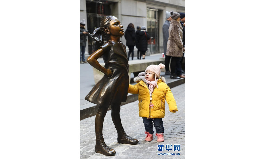 12月10日，在美国纽约，一名小女孩端详纽约证券交易所前的“无畏女孩”铜像。  新华社记者 王迎 摄