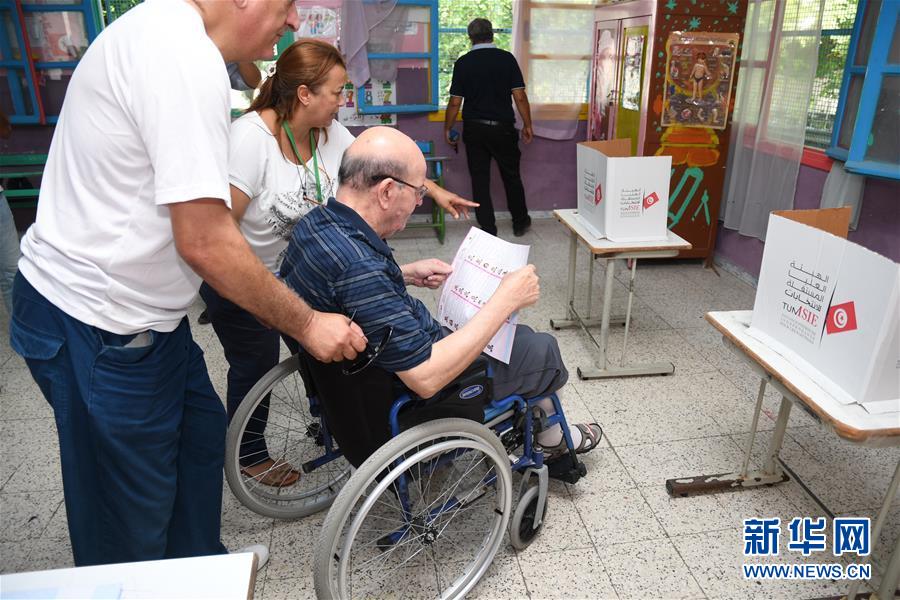 9月15日，在突尼斯首都突尼斯市，一名选民在工作人员的帮助下参加投票。 当地时间15日上午8时，突尼斯总统选举投票开始，全国4567个投票中心的投票站向700多万登记选民开放。 新华社发（阿代尔摄）