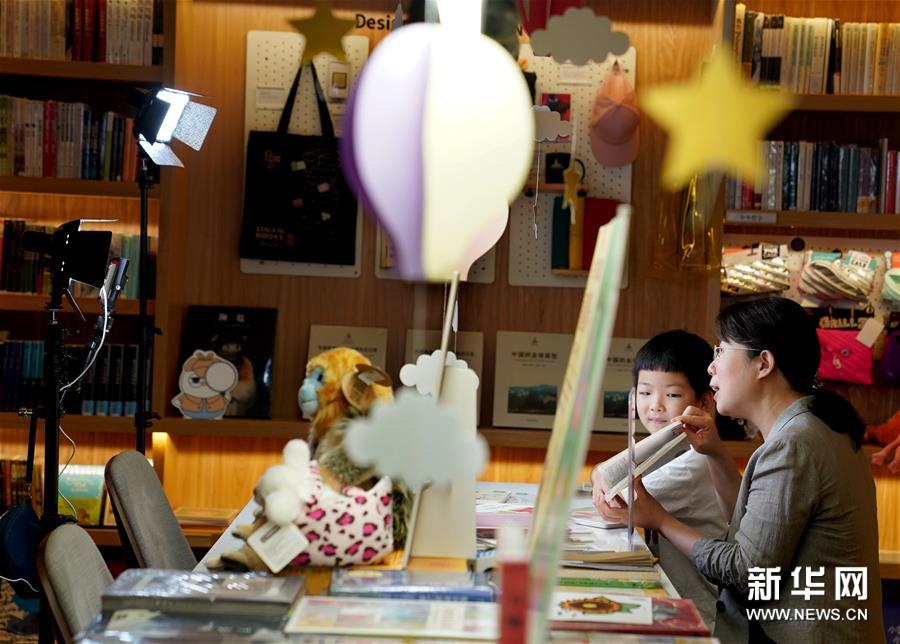 2020年6月1日，一场充满书香与童趣的“纯真预言”儿童节主题直播在上海思南书局举行。热爱阅读的小朋友变身“小主播”，带领大小网友们“云”逛书店，分享自己喜欢的图书，并和图书作家互动交流。图为6月1日，在上海思南书局复兴中路店的亲子阅读区，7岁的小读者果果与儿童文学作家、魔法童书会创始人张弘一同参与绘本阅读直播。 新华社记者 刘颖 摄