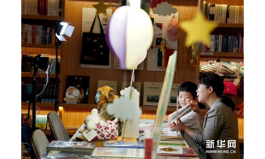 2020年6月1日，一场充满书香与童趣的“纯真预言”儿童节主题直播在上海思南书局举行。热爱阅读的小朋友变身“小主播”，带领大小网友们“云”逛书店，分享自己喜欢的图书，并和图书作家互动交流。图为6月1日，在上海思南书局复兴中路店的亲子阅读区，7岁的小读者果果与儿童文学作家、魔法童书会创始人张弘一同参与绘本阅读直播。 新华社记者 刘颖 摄