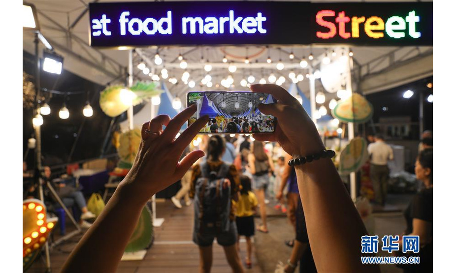 8月10日，在泰国曼谷河滨夜市，一名游客用手机拍照。 夜幕之下，多姿多彩的夜生活让曼谷这座城市充满活力。 新华社记者 张可任 摄