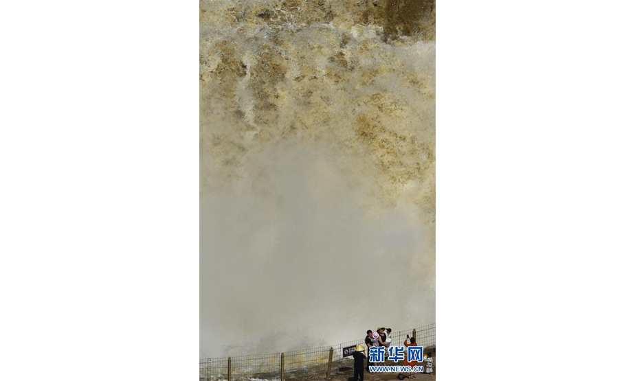 6月30日，游客在山西吉县黄河壶口瀑布景区游览拍照。 受近期上游降雨增多影响，黄河干流进入汛期，壶口瀑布主副瀑布连成一线，再现壮美瀑布群。 新华社发（吕桂明 摄）