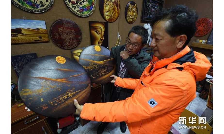 5月6日，申洪杰（左）在敦煌市沙州市场的工作室内向顾客介绍敦煌木刻画作品《鸣沙山·月牙泉》。 新华社记者范培珅摄 