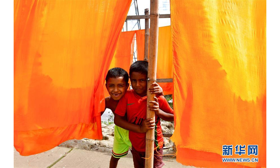 9月15日，在孟加拉国纳拉扬甘杰地区，两名儿童站在晾晒的布匹旁。 在孟加拉国中部的纳拉扬甘杰地区，当地村庄还保留着手工印染的工艺。 新华社发（萨利姆摄）