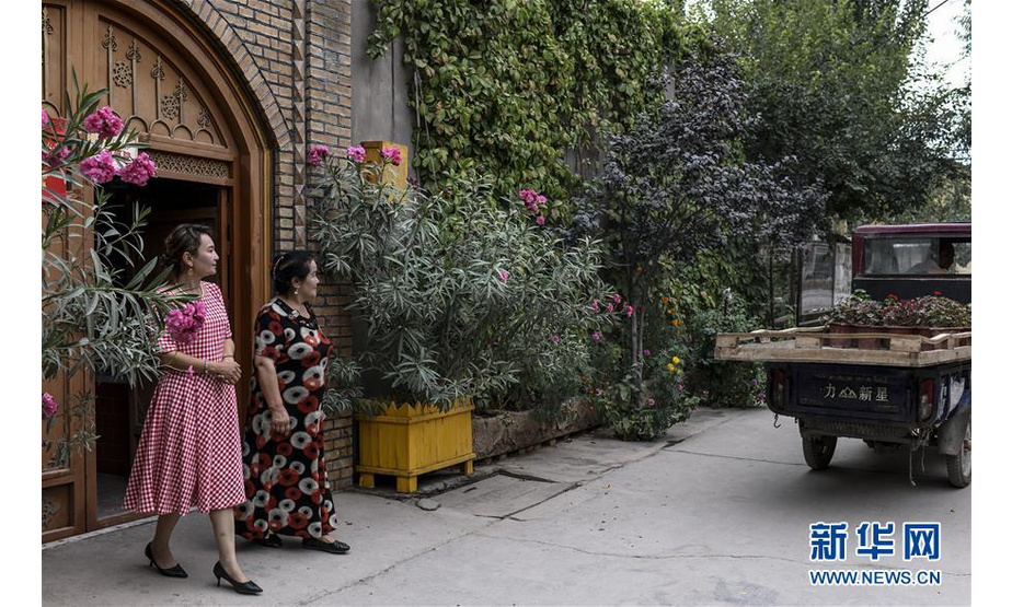 在新疆喀什市乃则尔巴格镇前进村，村民色里满·苏里坦（右）和女儿米热古丽·热夏提站在家门前，与花商告别（8月18日摄）。新华社记者 王菲 摄