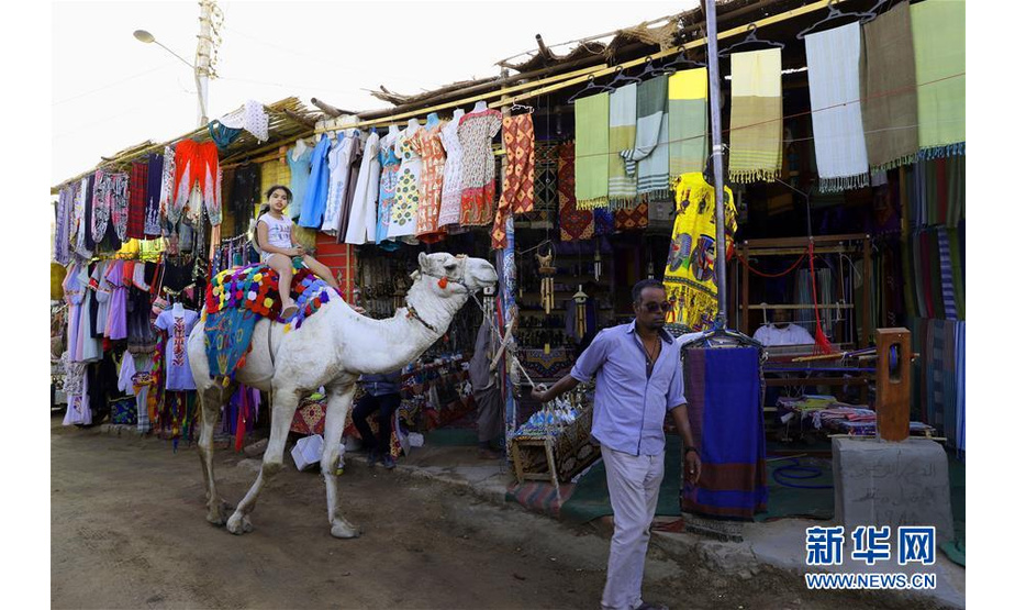 3月17日，在埃及阿斯旺，一名女孩骑着骆驼路过旅游市场店铺。 新华社发（艾哈迈德·戈马摄）