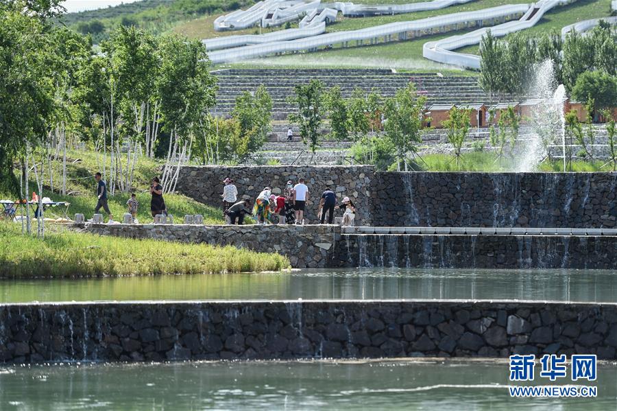 6月30日，游客在乌兰浩特市天骏山人工湖边游玩。 天骏山位于内蒙古自治区兴安盟乌兰浩特市郊区，曾因采挖石料而造成山体裸露，植被匮乏，山体上留下了多处深坑。近年来，当地政府加大生态修复力度，为天骏山增添绿色，将荒山改造成旅游景区，吸引游客前往游玩。 新华社记者 刘磊 摄