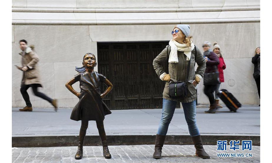 12月10日，在美国纽约，一名女士与纽约证券交易所前的“无畏女孩”铜像合影。  新华社记者 王迎 摄