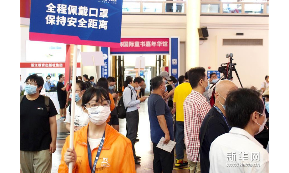 8月12日，在位于上海展览中心的2020上海书展主会场，志愿者举着防疫提示牌在展馆内行走。 新华社记者 任珑 摄