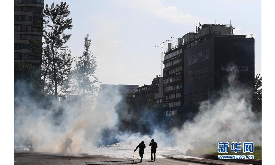 10月19日，在智利圣地亚哥，人们在街头参加抗议活动。 智利军方19日晚宣布在首都圣地亚哥实施宵禁，以避免因公交系统涨价引发的暴力抗议进一步升级。智利内政部长安德烈斯·查德威克20日说，首都圣地亚哥以外城市也出现了暴力破坏行为，康塞普西翁和瓦尔帕莱索市已进入紧急状态，他表示已经采取并将继续采取措施以保障社会秩序和公民安全。 新华社发（豪尔赫·比列加斯摄）