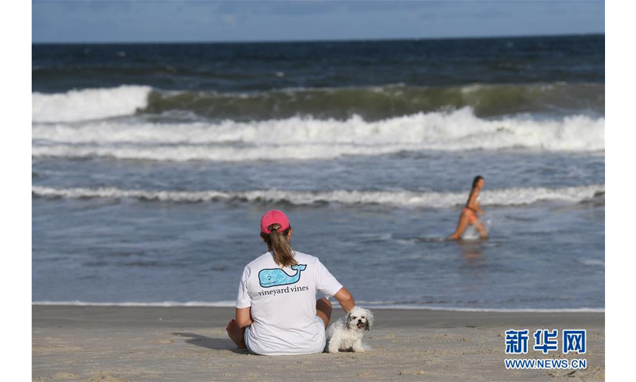 9月12日，在美国北卡罗来纳州威尔明顿市，一名女子带着宠物狗坐在沙滩上。 新华社记者 刘杰 摄 