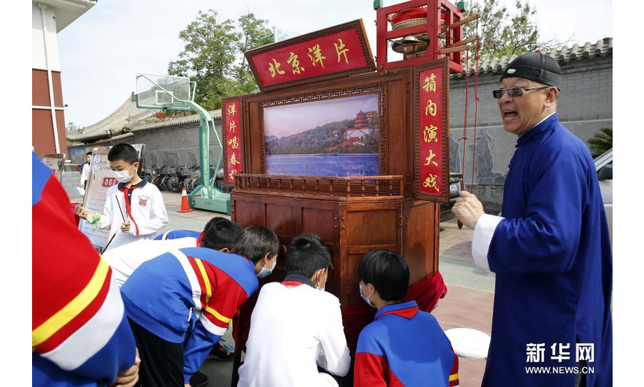 5月10日，学生们观看民间艺人展示的北京洋片。新华社发（周良 摄）