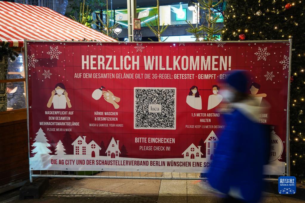 11月22日，在德国首都柏林的布赖特沙伊德广场，一名行人经过圣诞市场旁的防疫须知。

　　受新冠疫情影响，德国柏林、法兰克福等地的圣诞市场有的取消，有的在较为严格的防疫措施下开放。

　　新华社发（斯特凡·蔡茨摄）