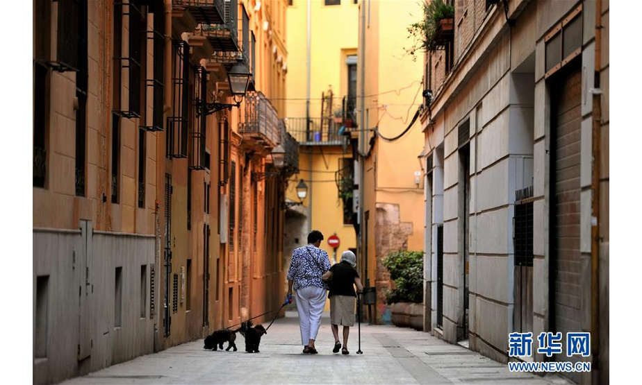 7月14日，在西班牙巴伦西亚，行人牵着狗走过小巷。 西班牙巴伦西亚紧靠大海，一年四季气候宜人。时值盛夏，游客纷纷来到这里度假，与当地居民一起享受悠闲夏日。 新华社记者 郭求达 摄