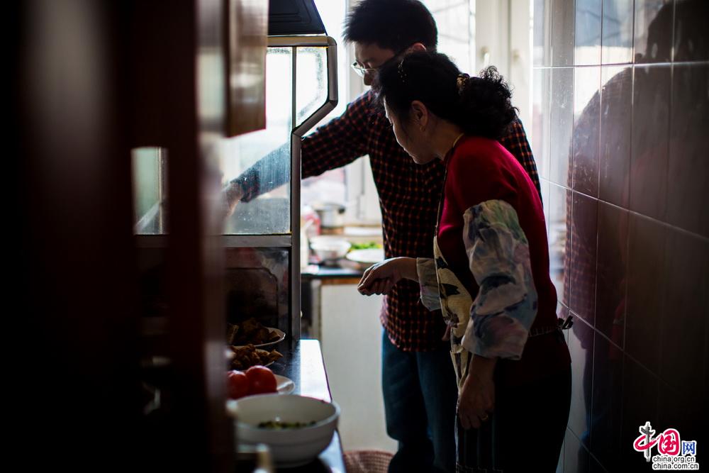 翻炒着锅里的青菜，妈妈在边上不住的指点，即便平日里自己也会做饭，但是在母亲眼里自己的每一个动作依旧是那么“笨拙”，即便如此，偷眼看过去母亲的脸上却是挂着笑容。中国网记者 郑亮 摄