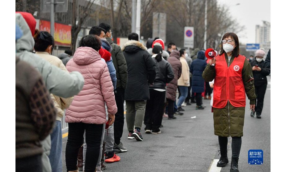 1月9日，在天津市南开区鼓楼街道一处核酸检测点，志愿者（右）用喇叭提醒市民核酸检测注意事项。新华社记者 孙凡越 摄