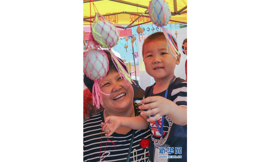 6月13日，在浙江省温州市鹿城区杨府山公园内，社区居民抱着孩子挑选蛋袋。端午节将至，人们开始包粽子、缝香囊，体验民俗活动，品味传统文化。 新华社发（苏巧将 摄）
