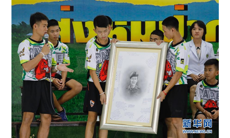 7月18日，在泰国清莱，从被困山洞中获救的少年足球队员捧着在救援行动中牺牲的泰国海军前士兵的肖像。 新华社发