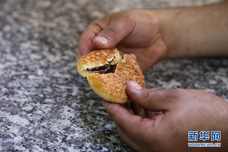 8月21日，在伊拉克巴格达一家面包店，面包师掰开烤制好的“克莱佳”。椰枣馅饼“克莱佳”是伊拉克的传统甜点，在庆祝节日或者家庭聚会时伊拉克人通常会将“克莱佳”配茶一起享用。“克莱佳”是用面粉和黄油或酥油制成的，形状和馅料多种多样，但椰枣馅最受欢迎。新华社发（哈利勒·达伍德摄）