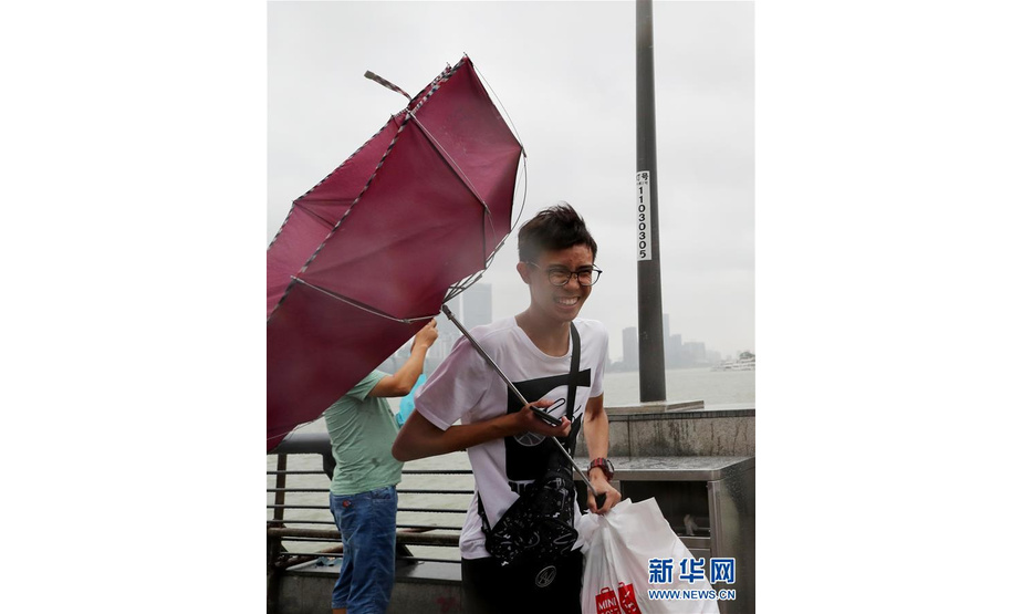 8月17日，在上海外滩，一位游客手中的雨伞在强风中变形。当日，今年第18号台风“温比亚”在上海浦东新区南部沿海登陆。受其影响，上海出现大风大雨天气。新华社记者 方喆 摄