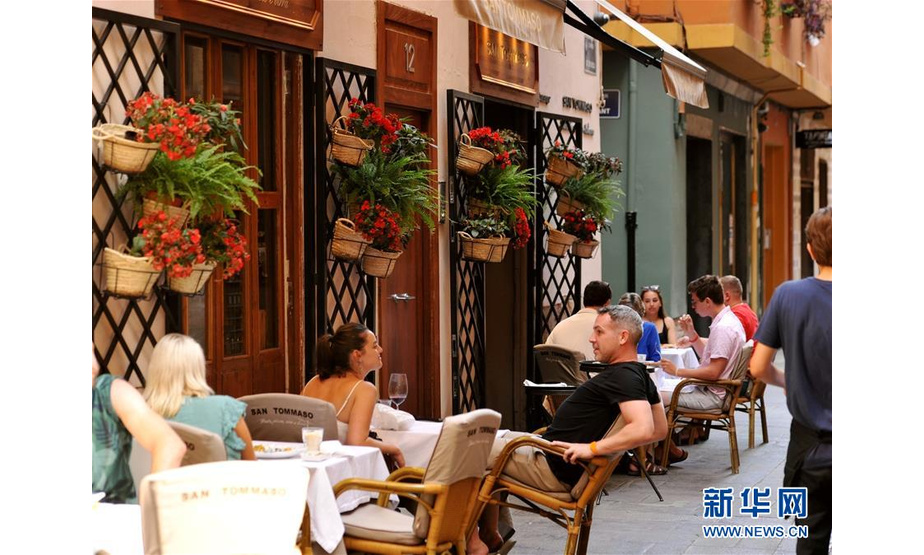 7月14日，在西班牙巴伦西亚，人们在街边餐厅吃饭聊天。 西班牙巴伦西亚紧靠大海，一年四季气候宜人。时值盛夏，游客纷纷来到这里度假，与当地居民一起享受悠闲夏日。 新华社记者 郭求达 摄