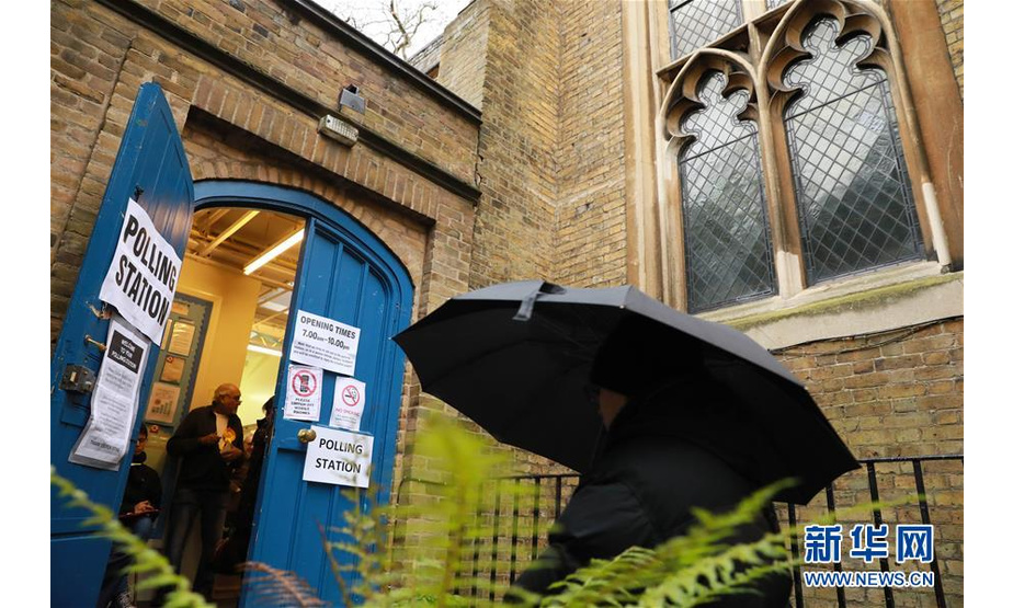 12月12日，在英国伦敦，行人撑伞走在一处投票站门前。 英国议会下院选举投票于当地时间12日7时开始。此次选举被称为“决定命运”的一次选举。 新华社发（蒂姆·爱尔兰 摄）