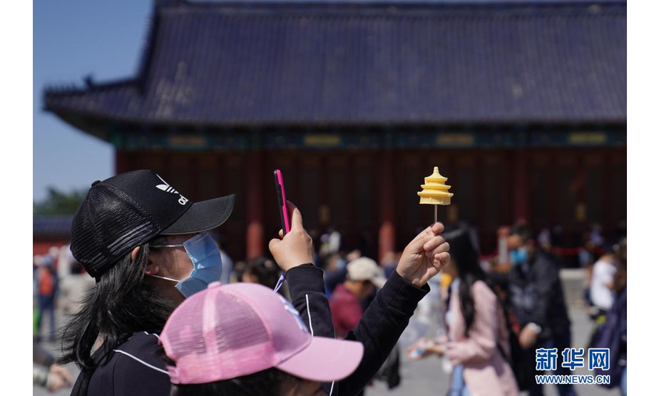 5月4日，游客在北京天坛公园祈年殿前拍摄祈年殿形状的雪糕。文化和旅游部5月5日晚间公布2021年“五一”假期旅游市场数据。统计显示，5月1日至5日，全国国内旅游出游2.3亿人次，同比增长119.7%，按可比口径恢复至疫前同期的103.2%。新华社记者 鞠焕宗 摄