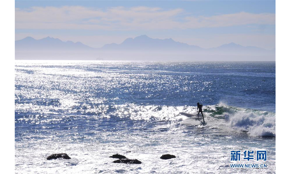 2019年5月2日，冲浪者在南非莫塞尔湾的海滨乘浪前行。 6月5日是第47个联合国世界环境日，今年的主题为“关爱自然 刻不容缓”。 新华社发（孙茵摄）
