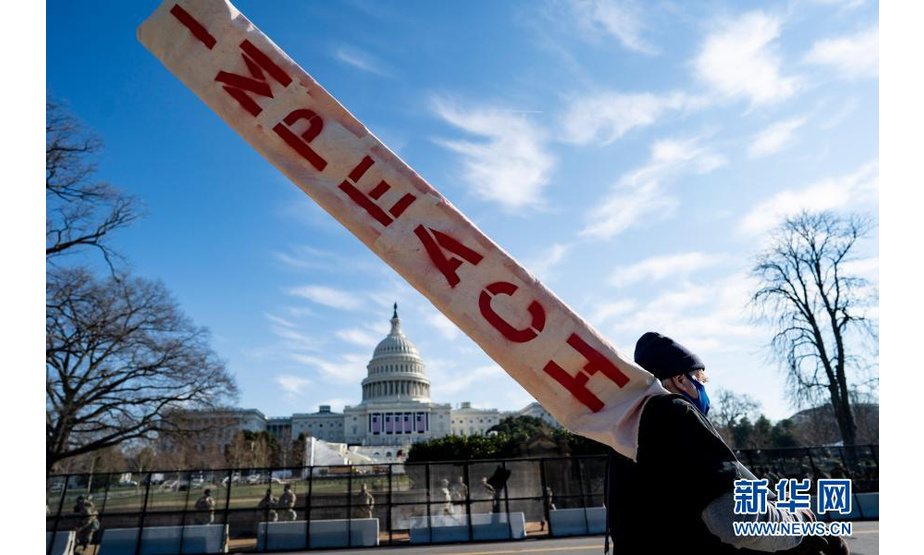 1月13日，在美国首都华盛顿，一名手持“弹劾”标语的男子从国会大厦前走过。新华社记者 刘杰 摄