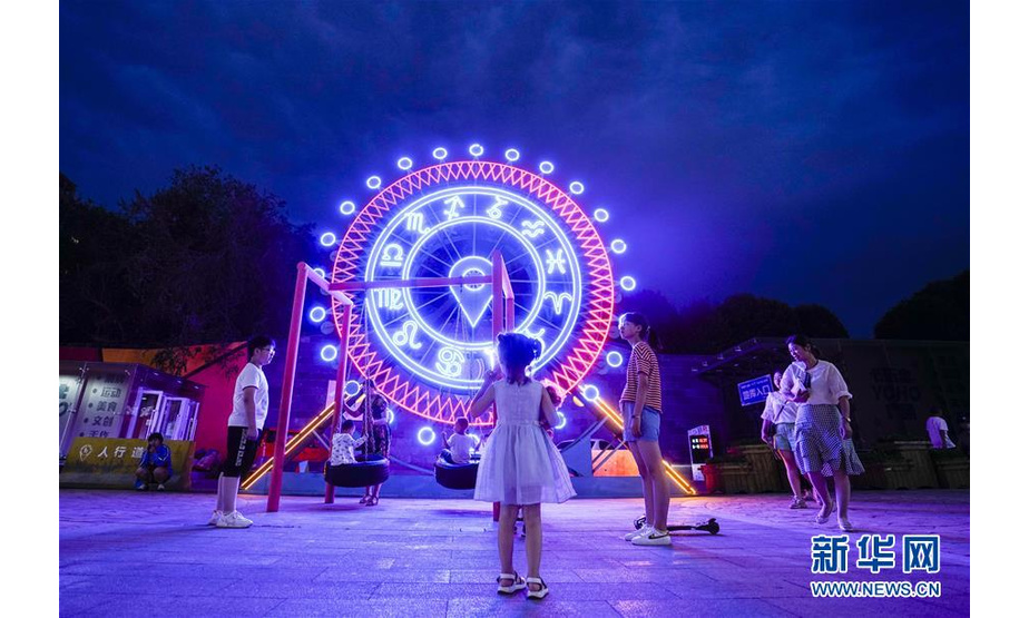 在乌鲁木齐街头，小朋友们在一座钟表模型下玩耍（7月14日摄）。 进入7月，乌鲁木齐的夜间经济逐渐升温。市民和游客外出购物休闲、品味美食，享受凉爽夏夜的闲适生活。 新华社记者 赵戈 摄