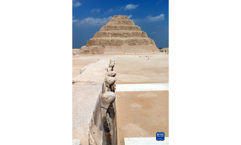 这是9月14日在埃及首都开罗以南的塞加拉地区一座左塞尔时期古墓的地上建筑拍摄的眼镜蛇雕像，以及远处的阶梯金字塔。

　　当日，位于埃及首都开罗以南约30公里的塞加拉地区，一座距今4000多年的古埃及第三王朝国王左塞尔时期的古墓经过近15年的修缮后正式向公众开放。该墓位于左塞尔王阶梯金字塔建筑群西南角，由地上建筑和地下墓室两大部分构成。埃及于2006年启动对该墓墓道、墓墙、墓室等建筑体的保护和修缮工作。

　　新华社记者 隋先凯 摄
