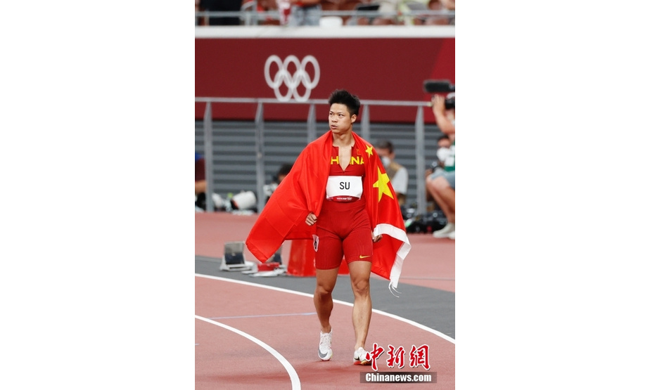 北京时间8月1日晚，在东京奥运会男子百米决赛中，中国选手苏炳添以9.98秒的成绩获得第六名，作为首位闯进奥运男子百米决赛的中国人，他再次创造了历史。图为苏炳添在赛后身披国旗。中新社记者 韩海丹 摄