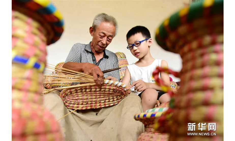 8月2日，杨振国在家中向小朋友介绍草编工艺品。新华社记者 朱旭东 摄
